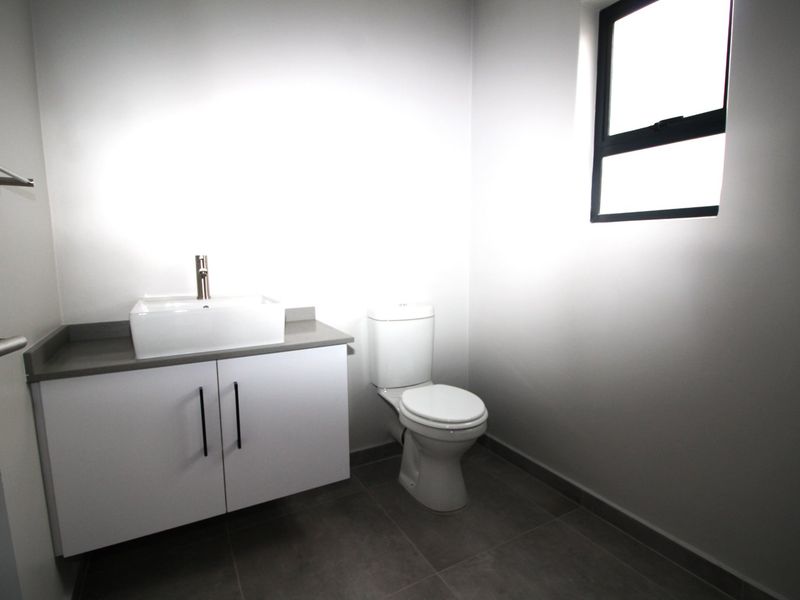 A clean, modern bathroom featuring a vanity with a vessel sink, a toilet, and neutral floor tiling.