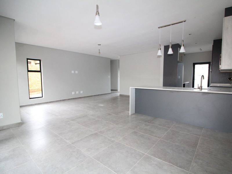 Spacious open-plan living and kitchen area featuring modern grey floor tiles, a central kitchen island, and contemporary pendant lighting throughout.