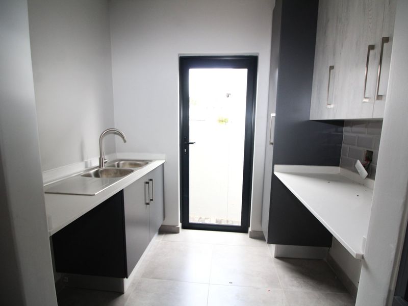A modern, clean scullery featuring double bowl sink, stone countertops, subway tile backsplash, and ample built-in cabinetry with direct access to the exterior.