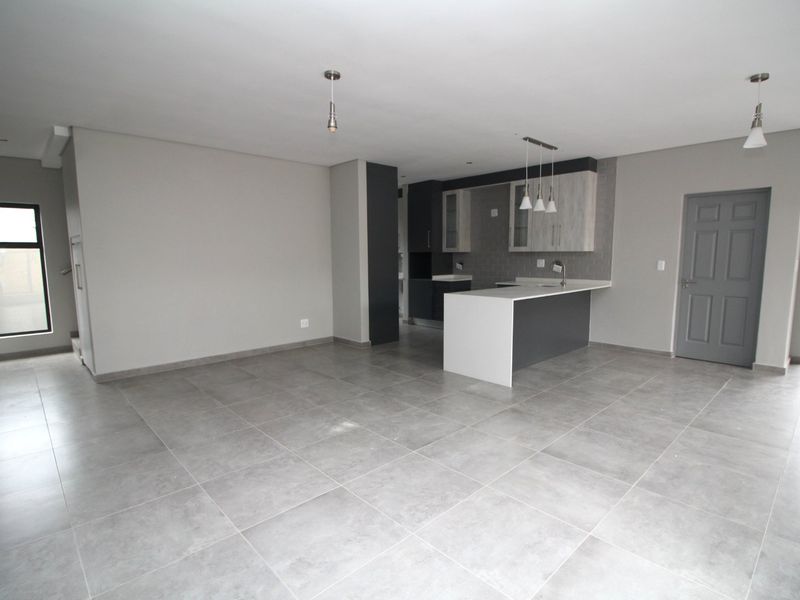 Spacious open-plan living area featuring modern tiled flooring, a contemporary kitchen with a central island, and neutral finishes throughout.