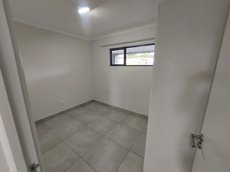 A clean, empty bedroom featuring neutral tiled flooring, white walls, and an aluminium-framed window, providing a blank canvas for personalization.