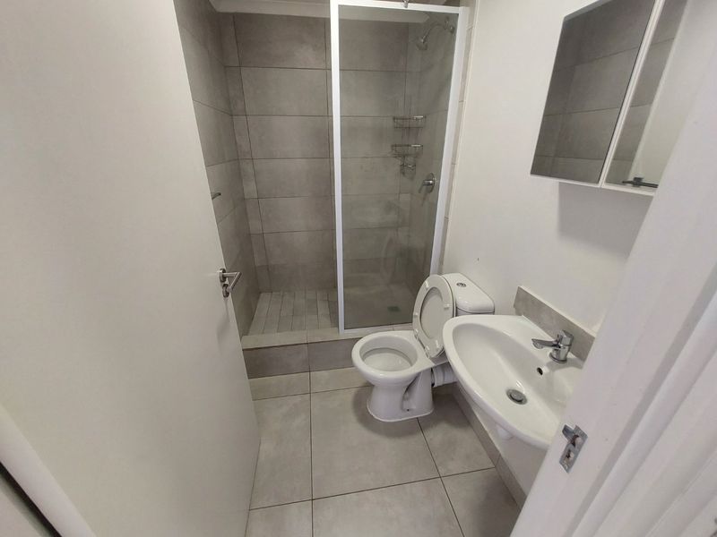 A clean, modern bathroom featuring a walk-in shower with glass enclosure, ceramic tiling, a wall-mounted basin, and a toilet.