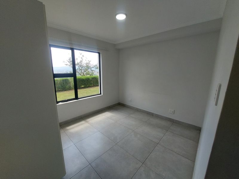A bright, empty bedroom featuring neutral tiled flooring, modern aluminium window frames, and clean finishes, offering a versatile space ready for personalization.