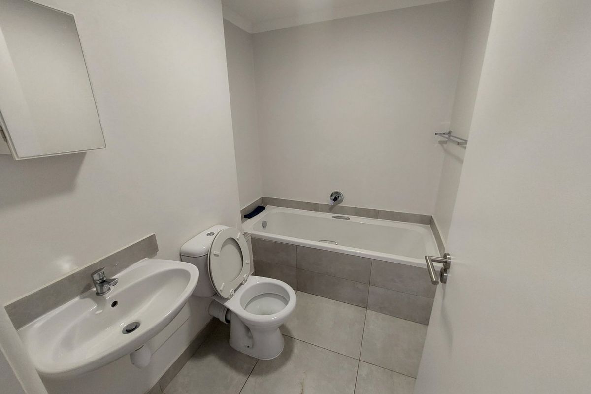 A clean, functional bathroom featuring a bathtub with tiled surround, pedestal sink, toilet, and neutral floor tiling.