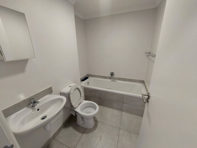 A clean, functional bathroom featuring a bathtub with tiled surround, pedestal sink, toilet, and neutral floor tiling.