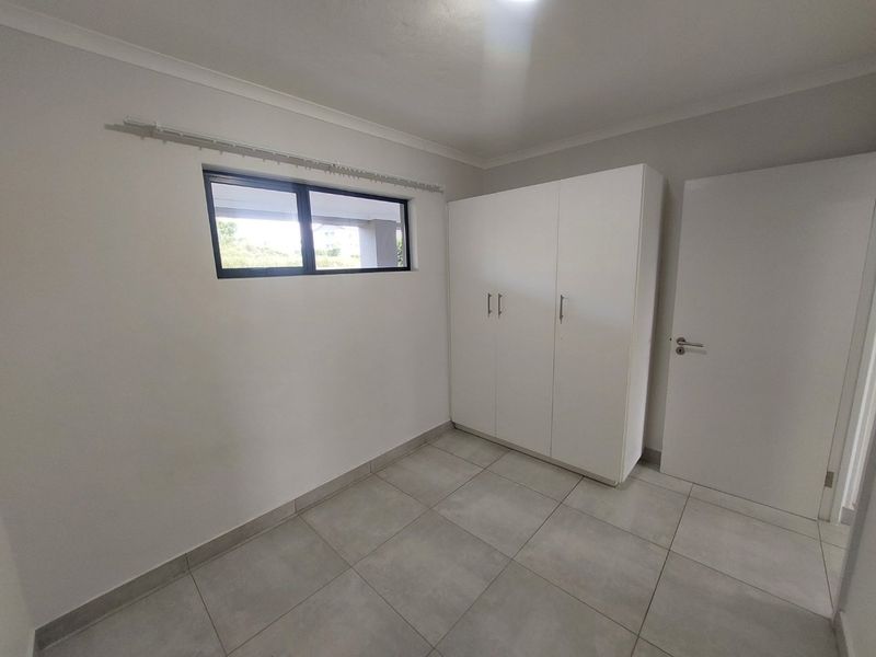 A clean, neutral bedroom featuring large floor tiles, a built-in wardrobe, and a modern aluminium window frame.
