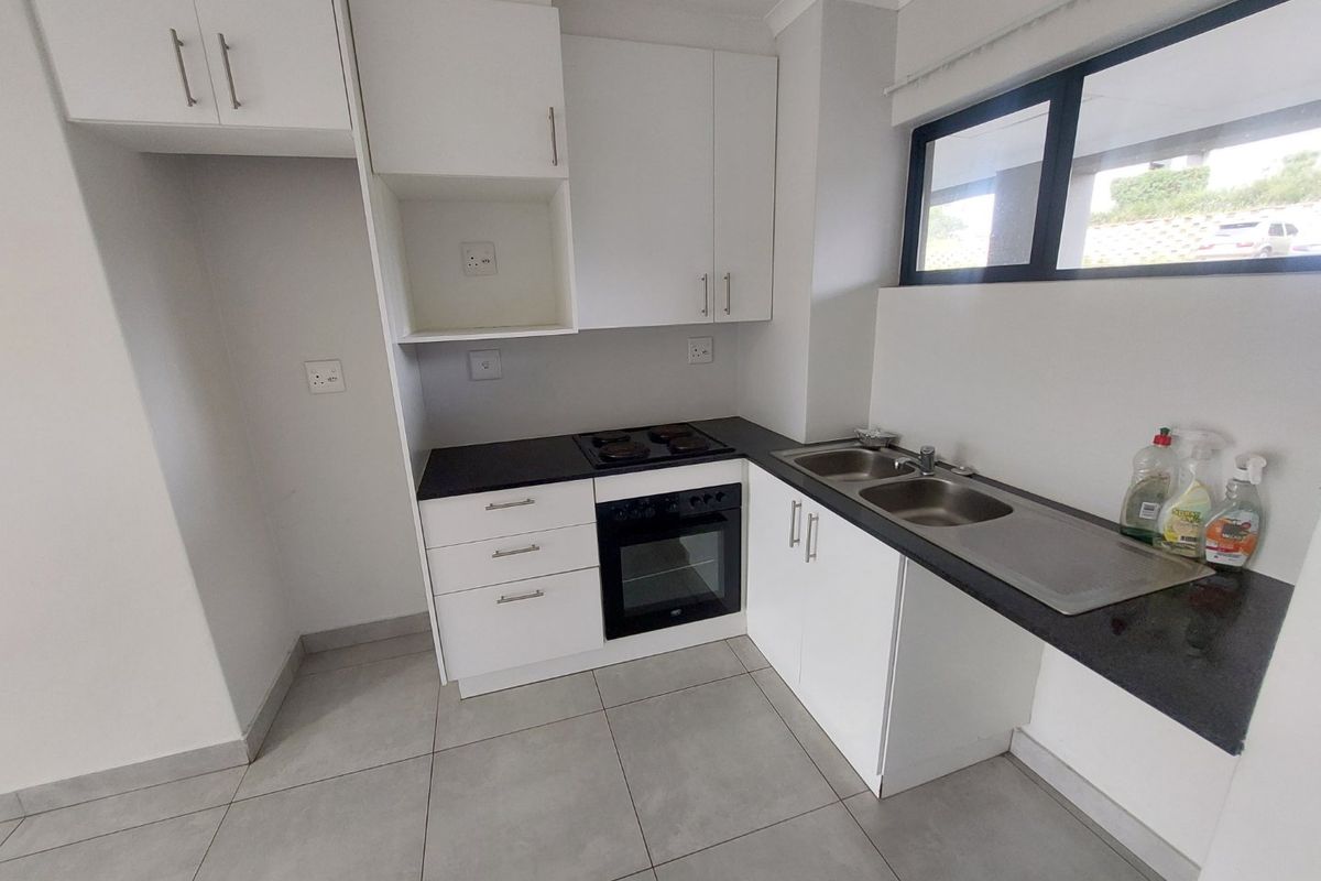 A clean, modern kitchen featuring white cabinetry, black granite countertops, a built-in oven and hob, and tiled flooring.