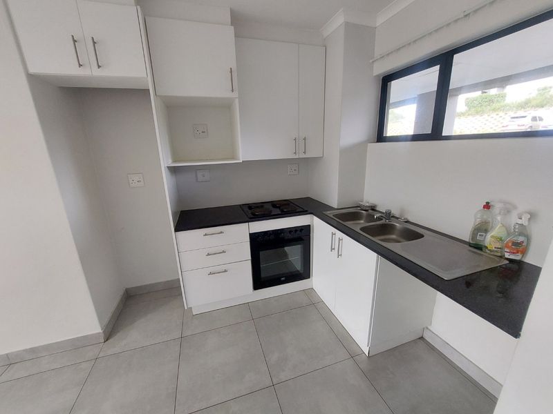 A clean, modern kitchen featuring white cabinetry, black granite countertops, a built-in oven and hob, and tiled flooring.