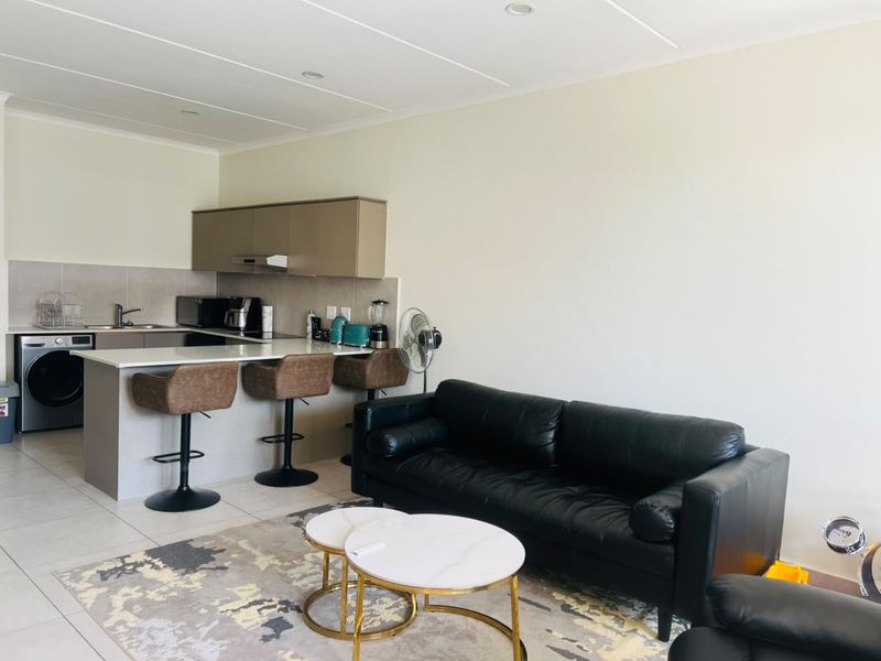 Open-plan living area featuring a modern kitchen with stone countertops, integrated cabinetry, and tiled flooring, seamlessly flowing into the lounge space.
