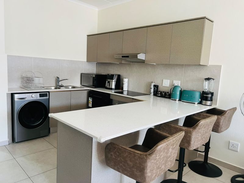 Modern kitchen featuring neutral cabinetry, stone countertops, integrated appliances, and a breakfast bar, providing a functional and contemporary cooking space.