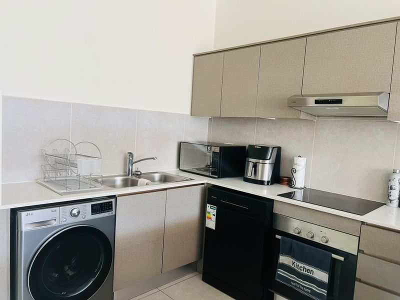 Modern kitchen featuring neutral cabinetry, tiled splashback, integrated oven, electric hob, extractor fan, and stainless steel sink with dedicated laundry appliance space.
