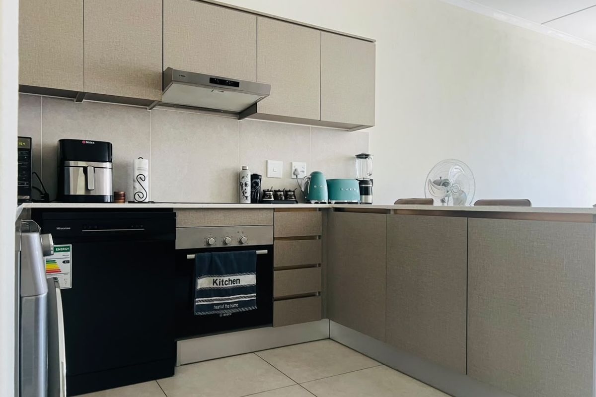 A modern kitchen featuring neutral-toned built-in cabinetry, stone countertops, an integrated oven, and an extractor fan with tiled flooring.