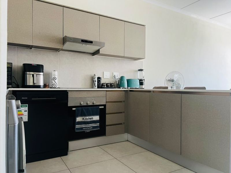 A modern kitchen featuring neutral-toned built-in cabinetry, stone countertops, an integrated oven, and an extractor fan with tiled flooring.