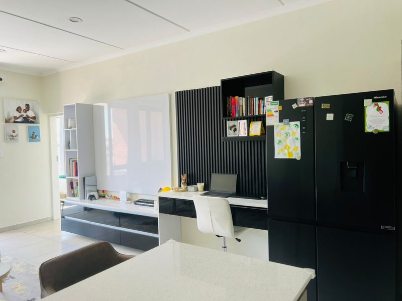 Open plan living area featuring modern built-in cabinetry, a dedicated desk space with decorative slatted wall paneling, and neutral tiled flooring.