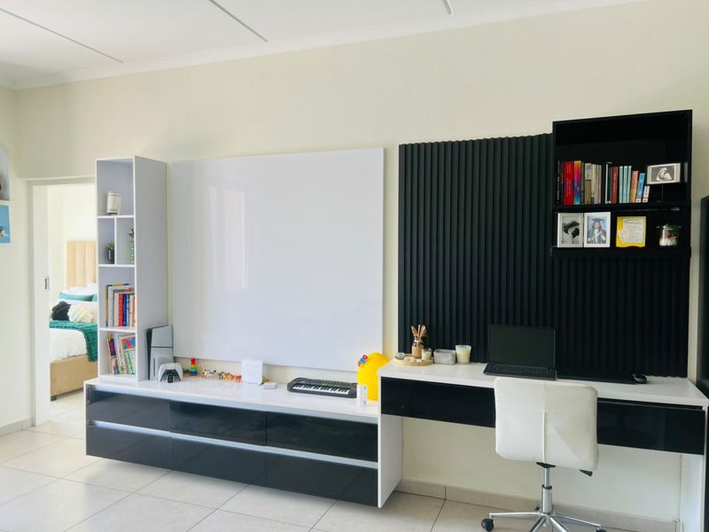 A modern living area featuring custom built-in cabinetry, a sleek desk workspace, and decorative slatted wall paneling with neutral tiled flooring.