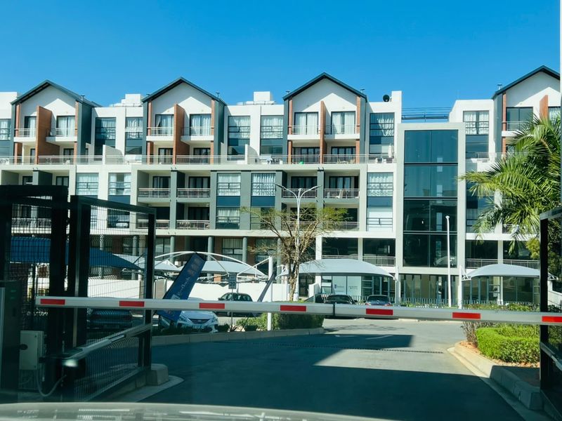 Front view of a modern multi-story apartment complex featuring a secure gated entrance, private balconies, and covered parking facilities.