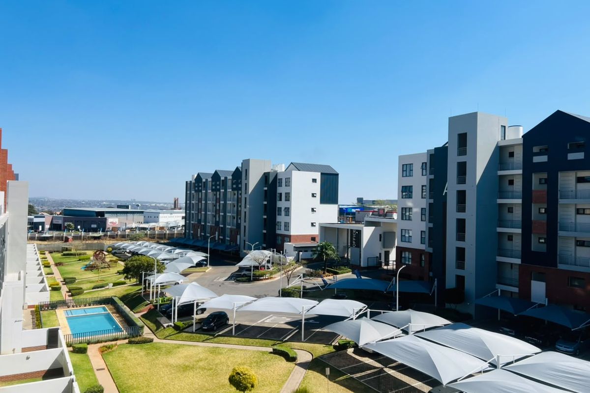 Aerial view of a modern apartment complex featuring landscaped gardens, a swimming pool, and extensive shade cloth parking facilities.