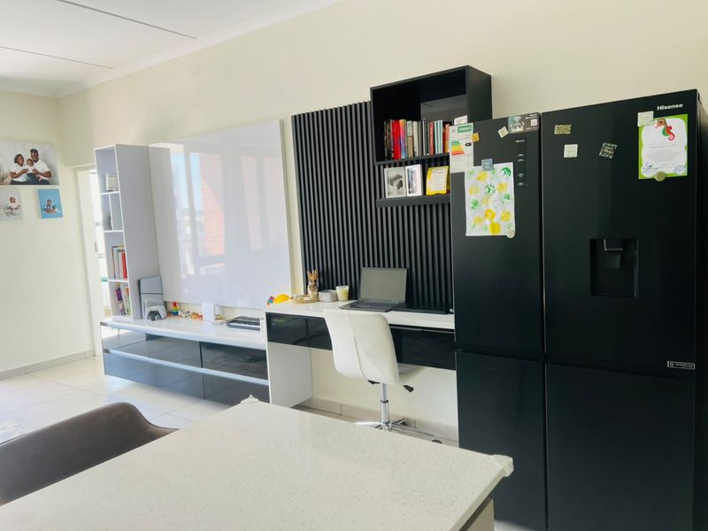 Open plan living area featuring modern built-in cabinetry, a dedicated desk space with decorative slatted wall paneling, and neutral tiled flooring.