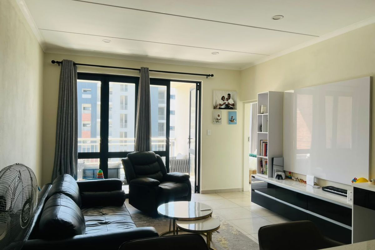 A bright living room featuring tiled floors, recessed lighting, and large sliding glass doors that open onto a balcony, with a modern built-in media unit.