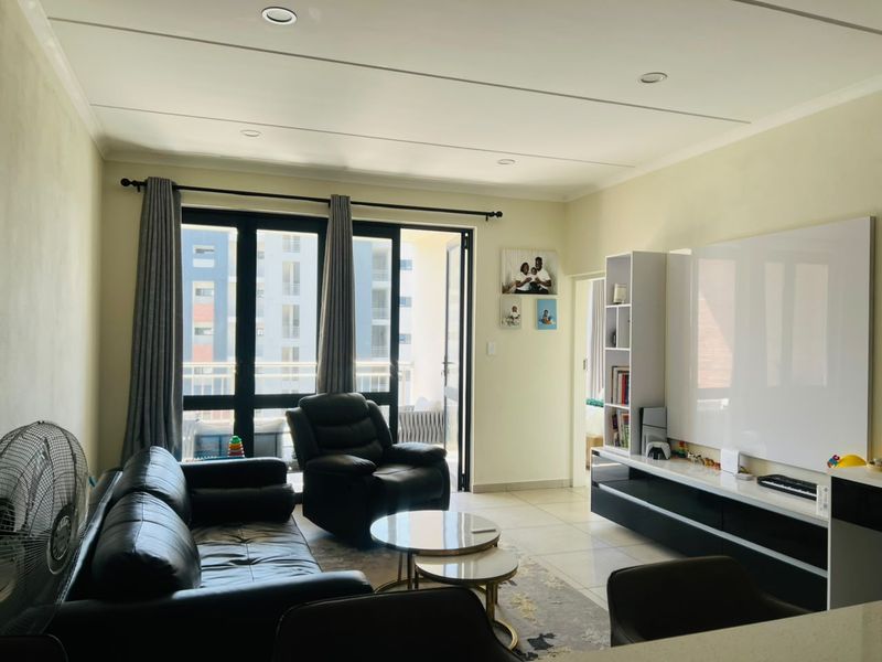 A bright living room featuring tiled floors, recessed lighting, and large sliding glass doors that open onto a balcony, with a modern built-in media unit.