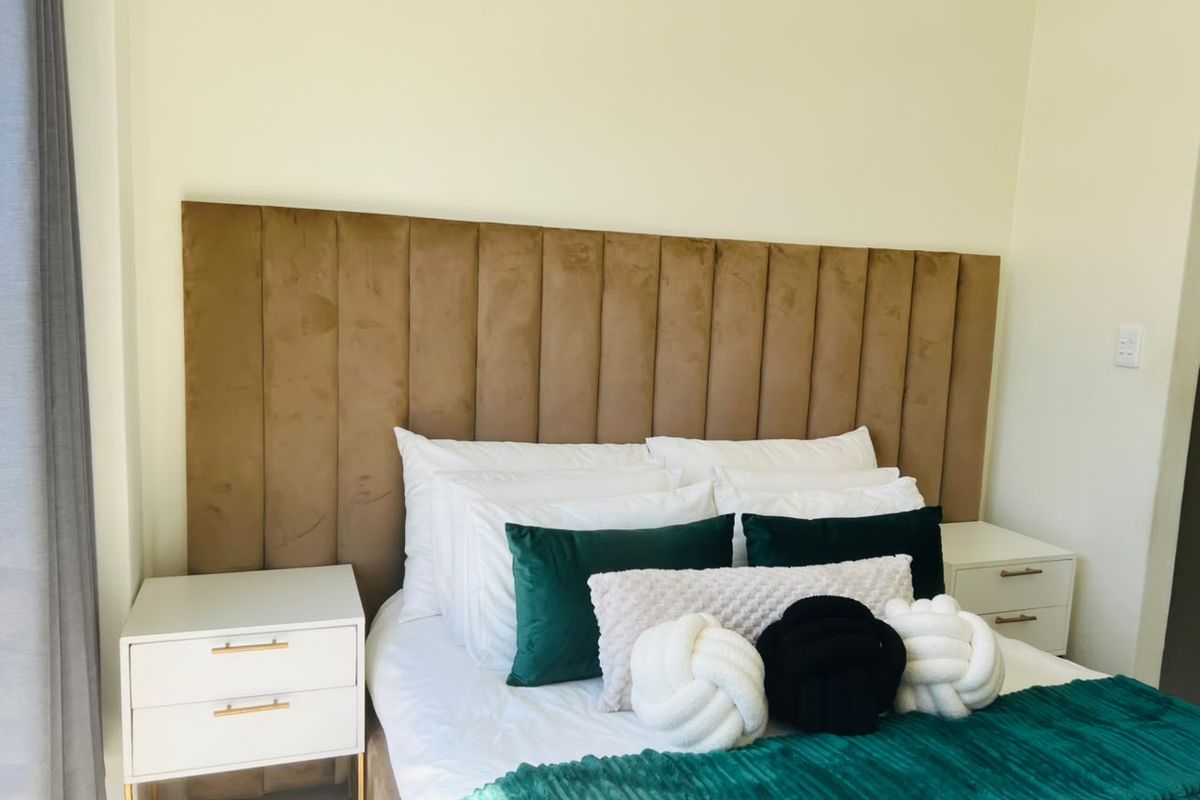 A well-presented bedroom featuring a modern, floor-to-ceiling upholstered headboard and neutral wall finishes.