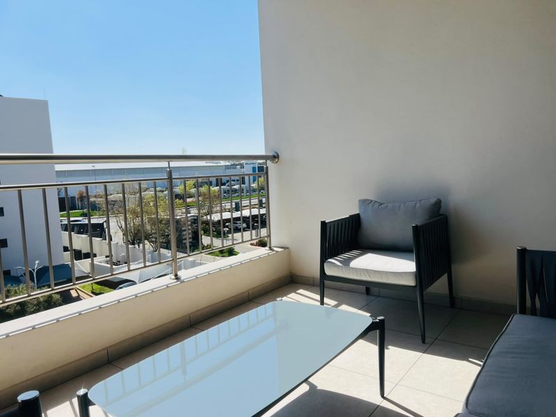 A bright, covered balcony featuring tiled flooring and a modern stainless steel balustrade, offering an open view of the surrounding area.