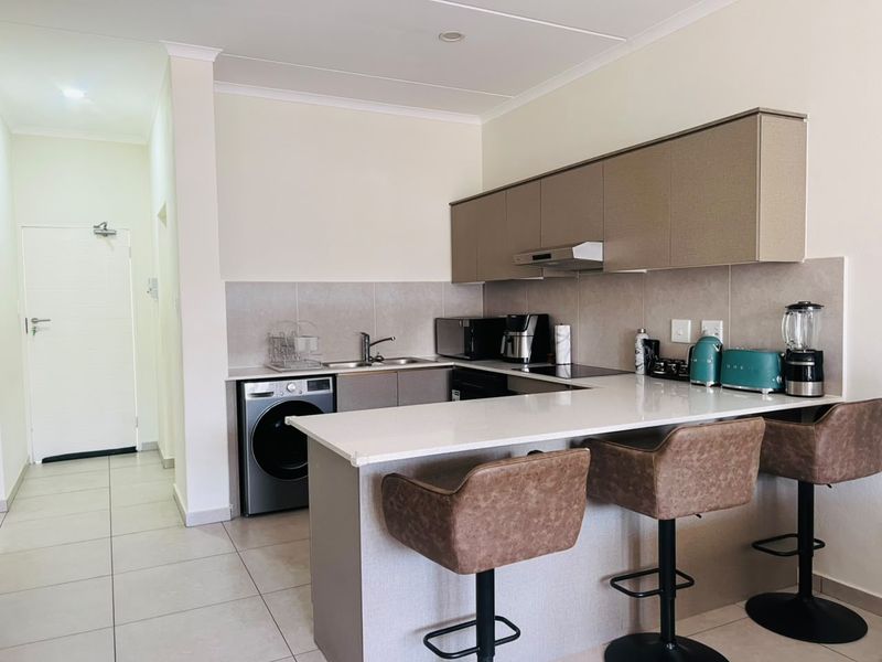 Modern kitchen featuring sleek built-in cabinetry, stone countertops, a breakfast bar, and integrated appliances, finished with neutral tiled splashbacks and flooring.