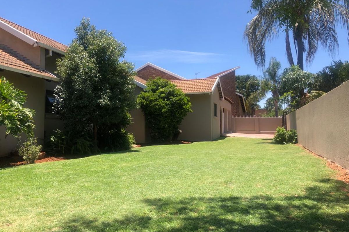 A well-maintained rear garden featuring a spacious lawn, established trees, and secure boundary walls, providing a private outdoor space.