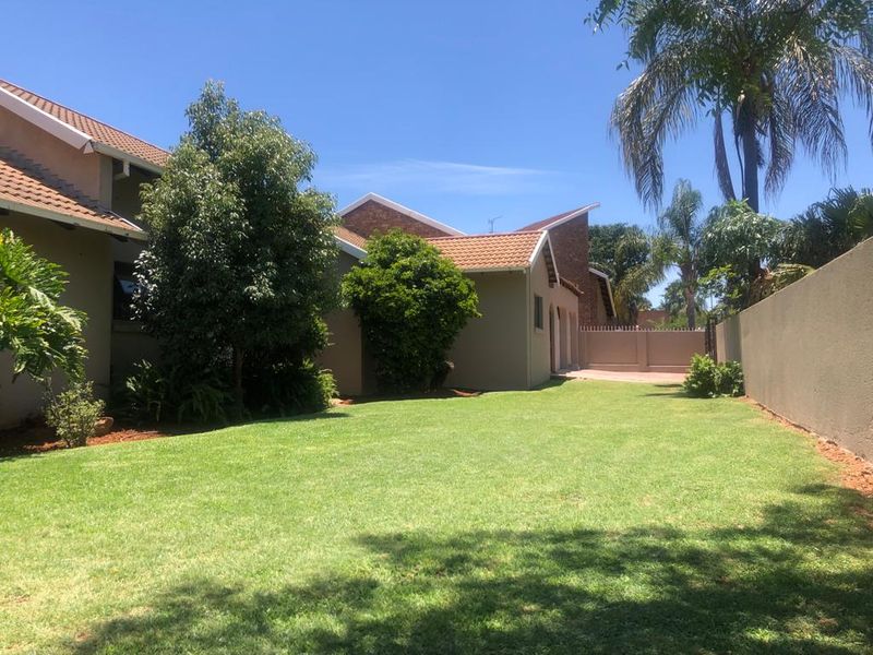A well-maintained rear garden featuring a spacious lawn, established trees, and secure boundary walls, providing a private outdoor space.