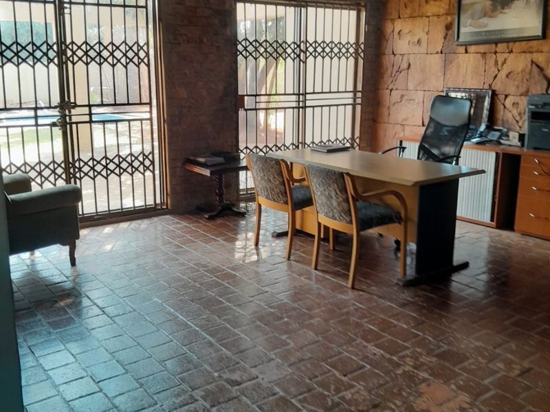A home office featuring rustic stone-clad walls, terracotta tile flooring, and large sliding glass doors with security gates leading to the exterior.