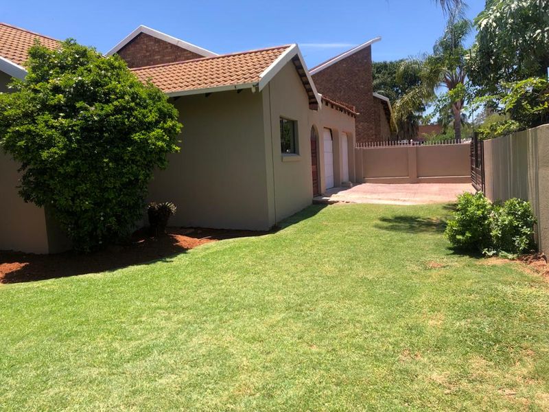 A view of the rear garden featuring a well-maintained lawn, paved driveway area, and brick perimeter walling.
