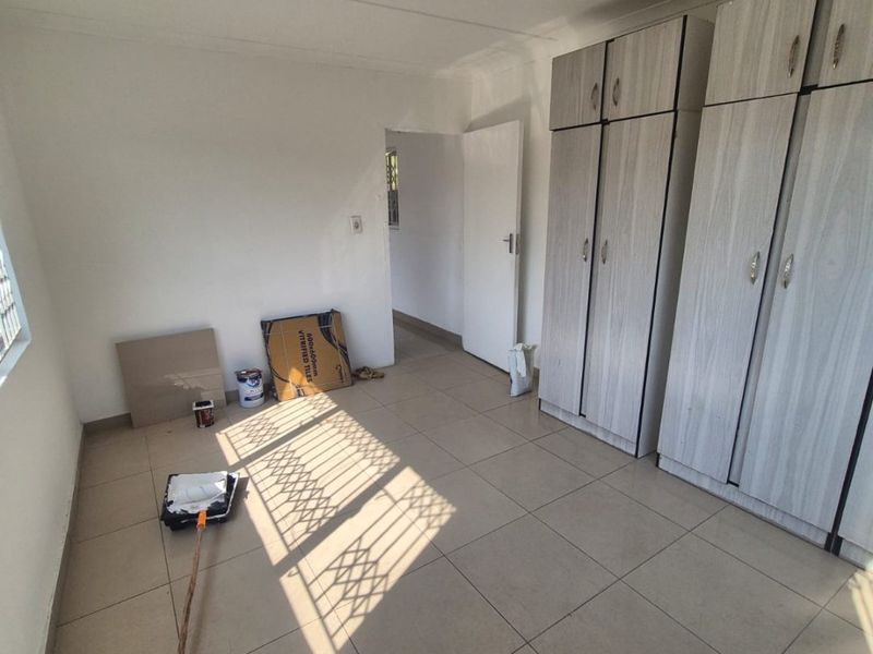 A bright, empty bedroom featuring neutral tiled flooring and built-in wooden cupboards, currently undergoing minor maintenance.
