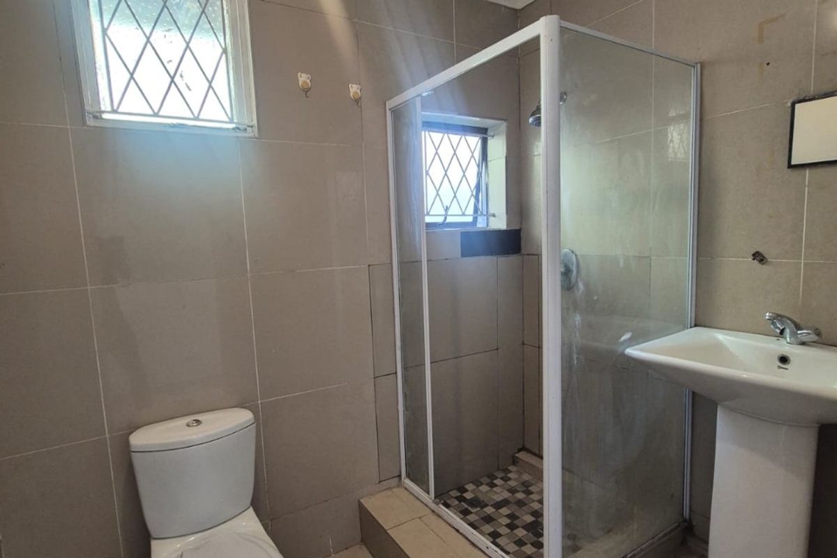 A functional bathroom featuring a pedestal basin, toilet, and a separate shower enclosure with tiled finishes throughout.