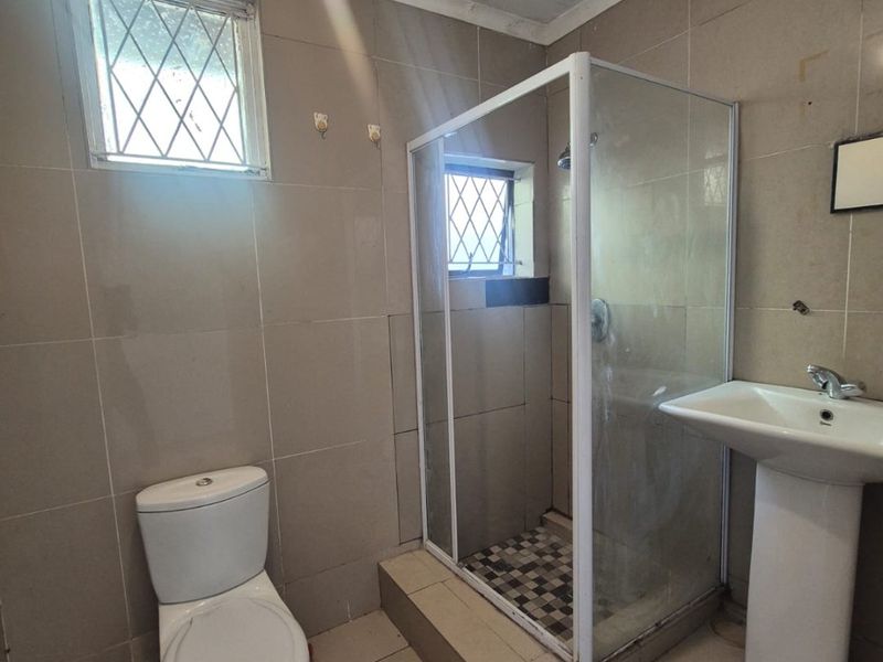 A functional bathroom featuring a pedestal basin, toilet, and a separate shower enclosure with tiled finishes throughout.