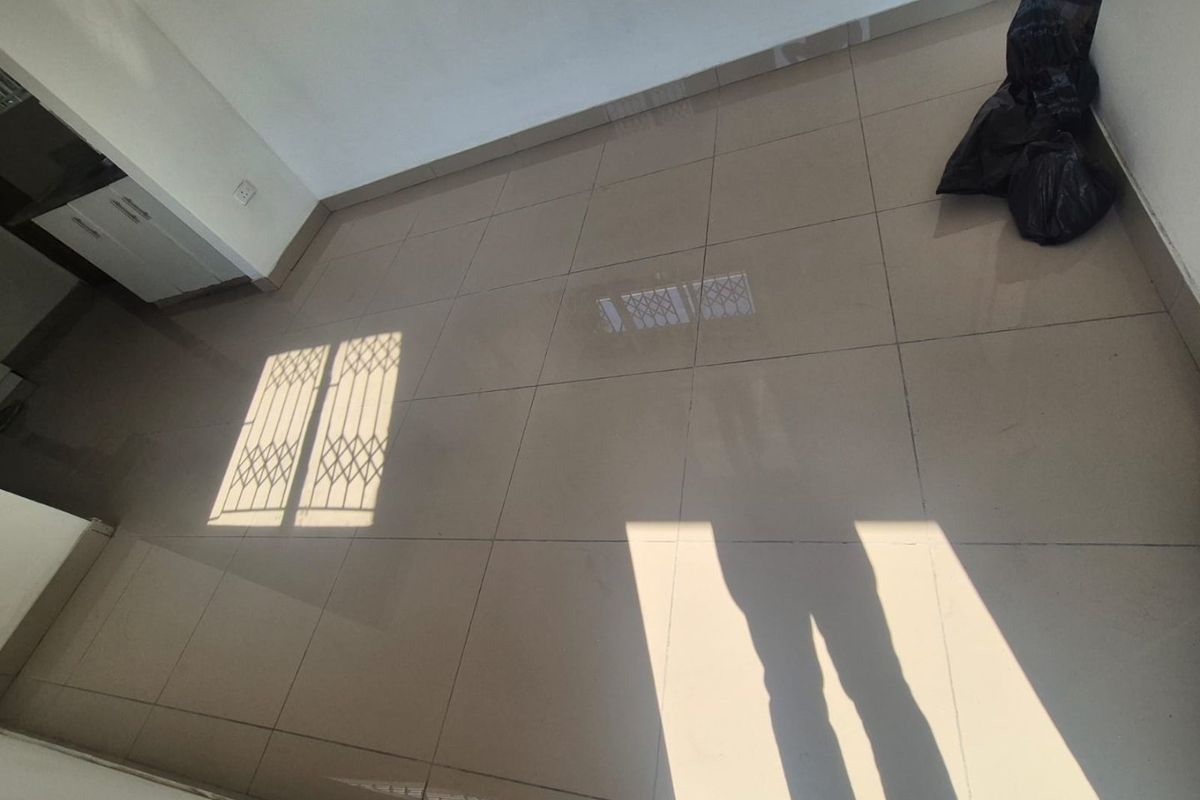 An empty, sunlit living area featuring neutral floor tiles and a security gate on the window.