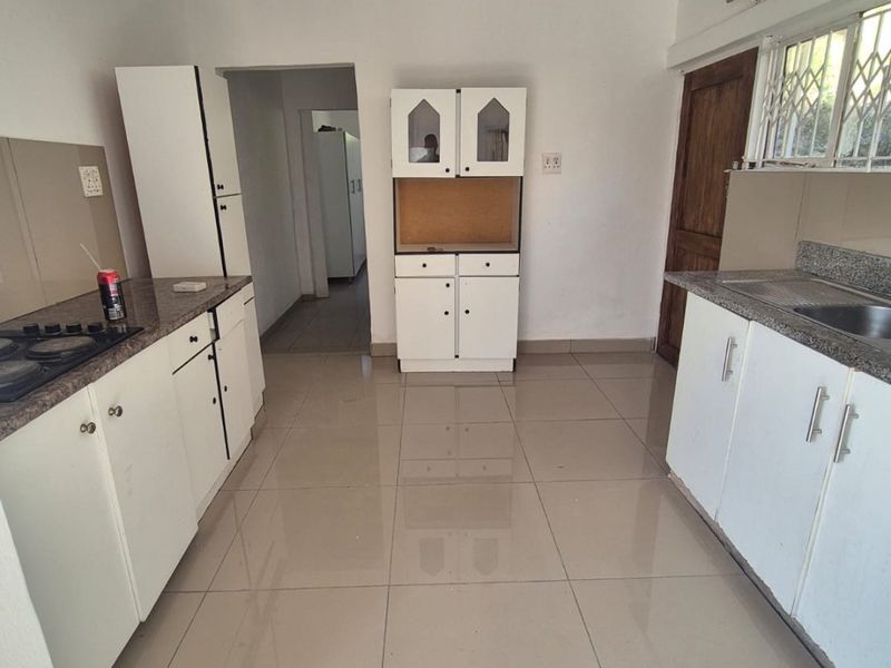 A functional kitchen featuring tiled flooring, granite countertops, built-in cabinetry, and a gas hob, offering a clean and practical workspace.