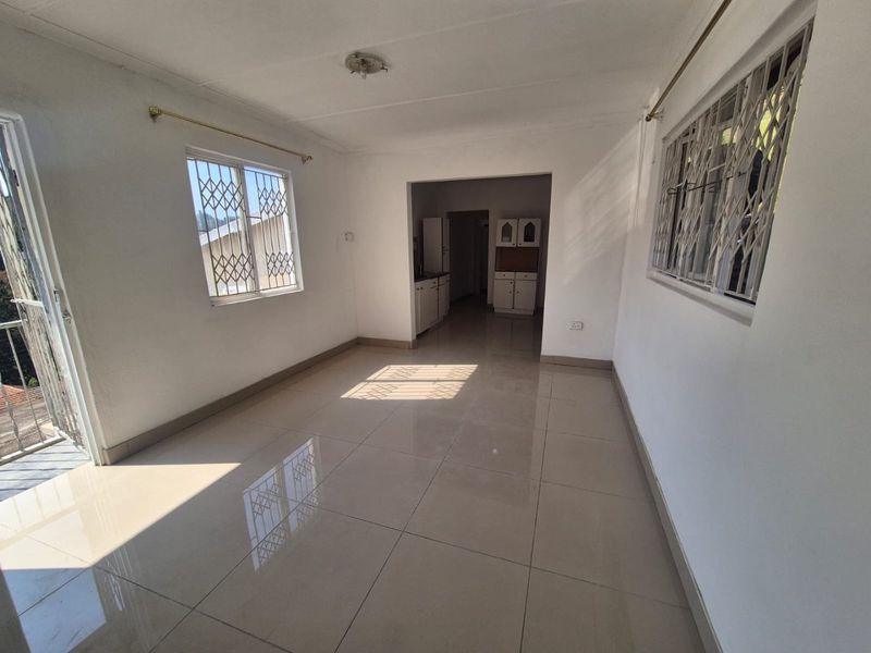 An open-plan living area featuring neutral tiled flooring, security gates on windows, and a view through to the adjacent kitchen space.