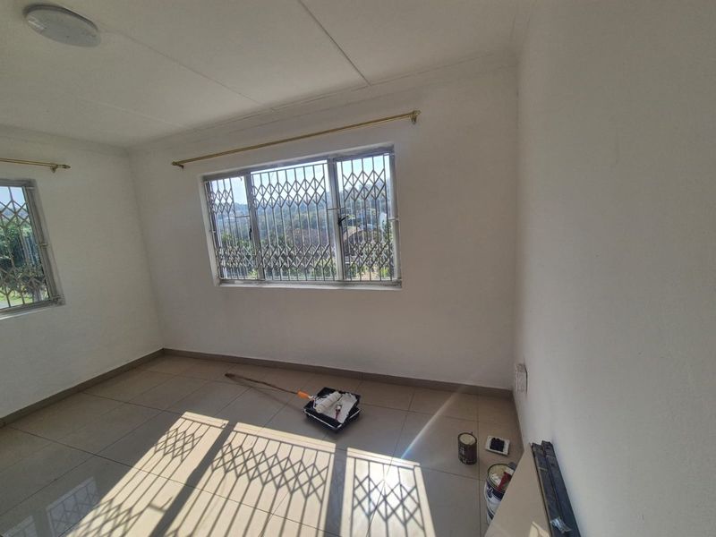 A bright, empty bedroom featuring tiled flooring, security gates on windows, and neutral walls, currently undergoing minor maintenance.