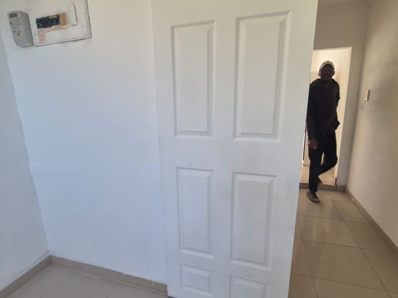 A simple hallway area featuring tiled flooring, a sliding door, and a wall-mounted electrical distribution board.