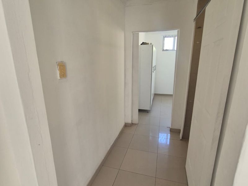 A narrow hallway featuring tiled flooring and a ceiling access hatch, currently showing signs of wear and requiring minor maintenance and finishing.