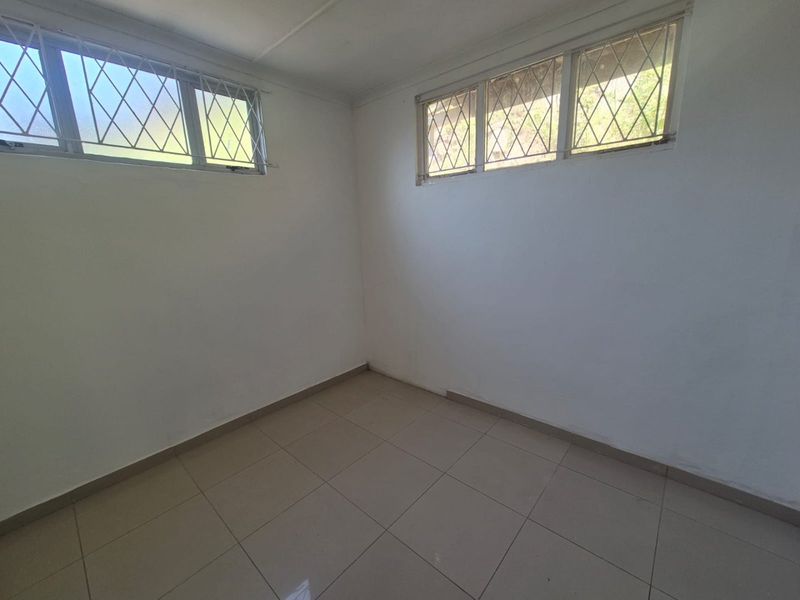 An empty bedroom featuring neutral tiled flooring and windows fitted with security bars, offering a clean and versatile space.