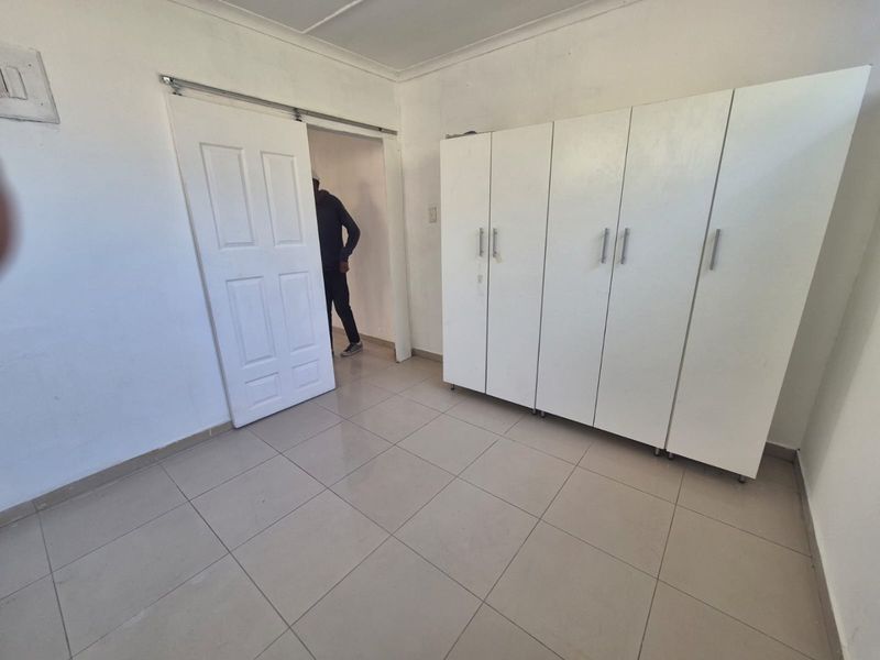 A clean, empty bedroom featuring neutral tiled flooring, white walls, and ample built-in cupboard storage space.