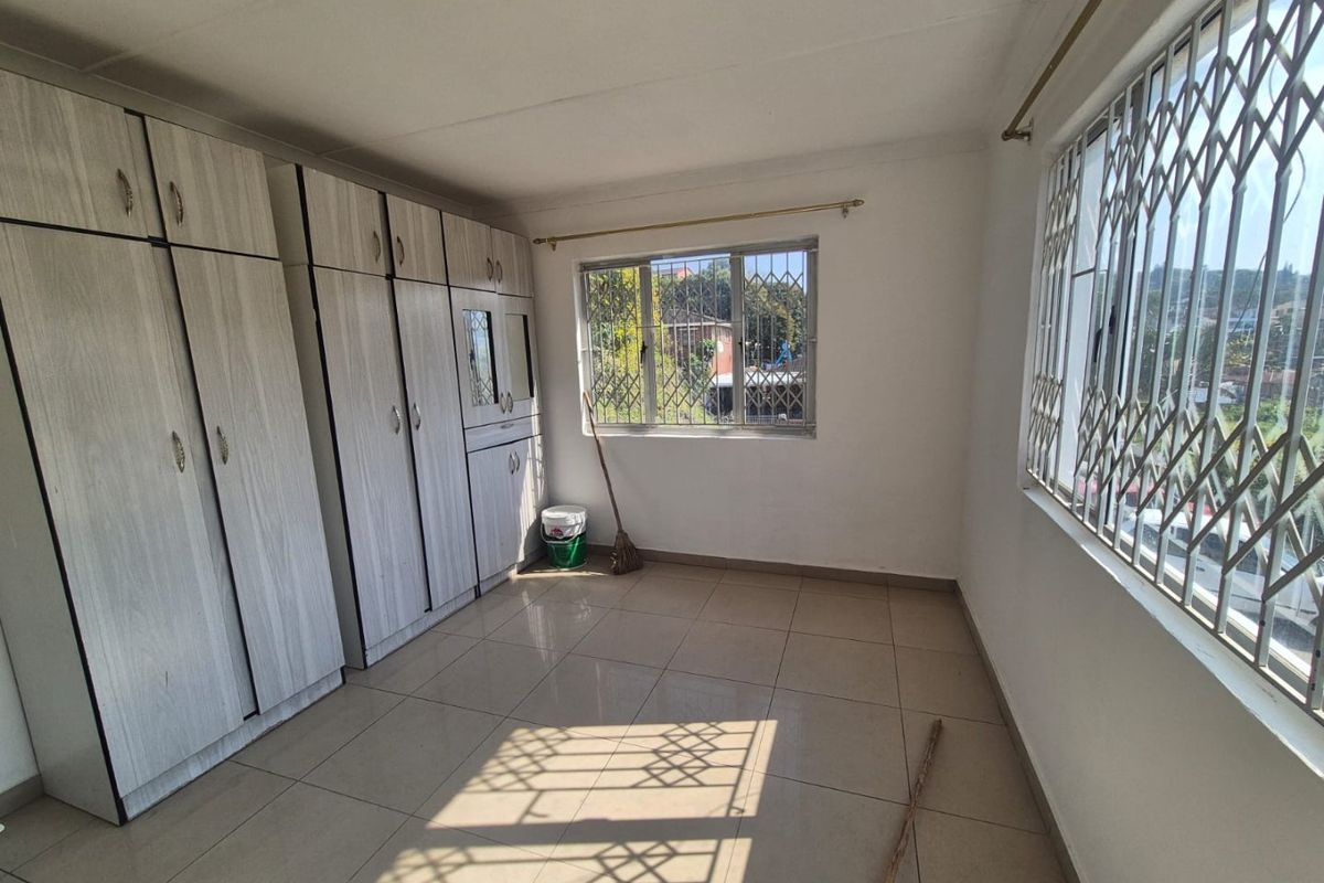 A bright, empty bedroom featuring neutral tiled flooring and extensive built-in cupboard storage, complemented by windows fitted with security bars.