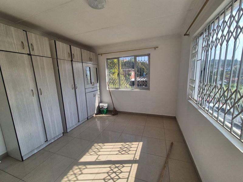 A bright, empty bedroom featuring neutral tiled flooring and extensive built-in cupboard storage, complemented by windows fitted with security bars.