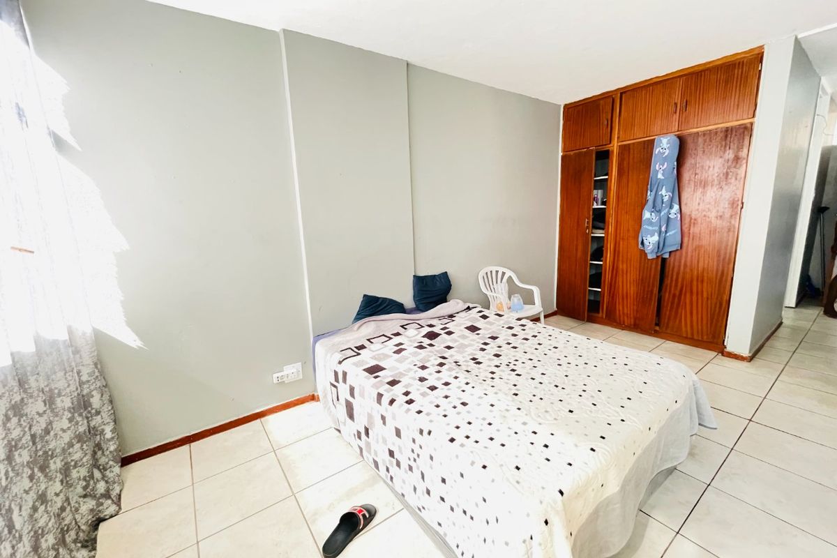 A bedroom featuring tiled flooring and a large built-in wooden wardrobe, offering functional storage space in need of cosmetic updates.