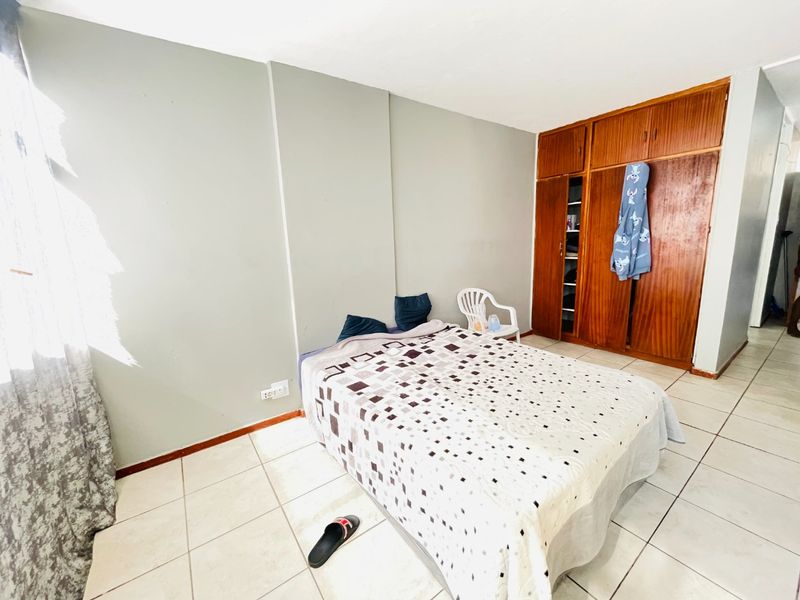 A bedroom featuring tiled flooring and a large built-in wooden wardrobe, offering functional storage space in need of cosmetic updates.