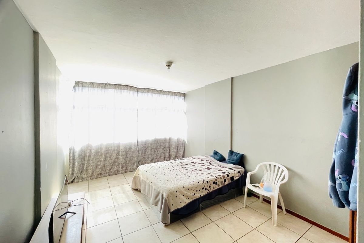 A simple bedroom featuring tiled flooring and a large window that allows for ample natural light.