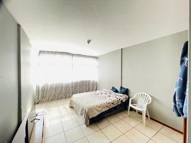 A simple bedroom featuring tiled flooring and a large window that allows for ample natural light.
