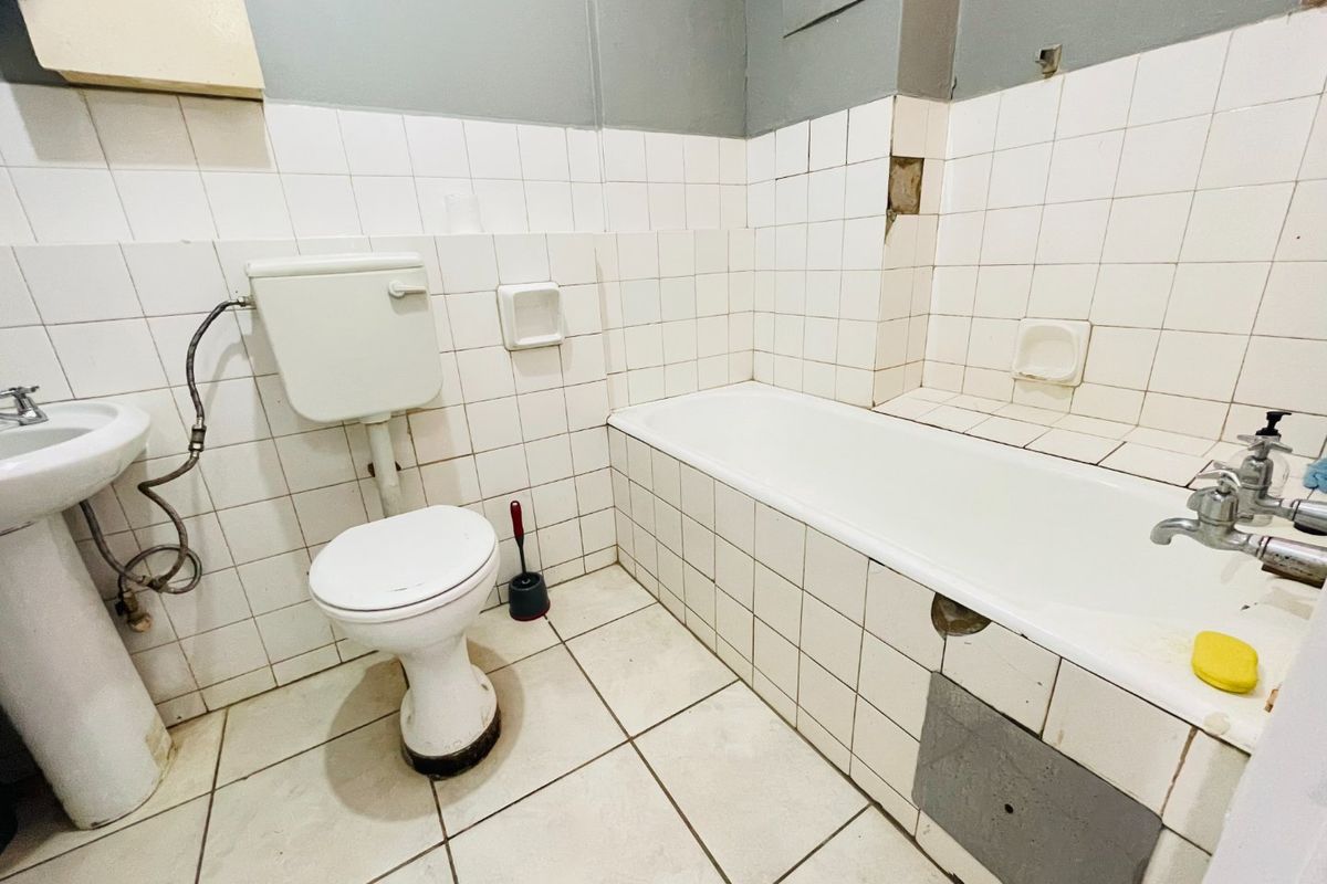 A dated bathroom featuring a pedestal basin, toilet, and bathtub with visible tile damage and maintenance requirements, offering potential for a full renovation.
