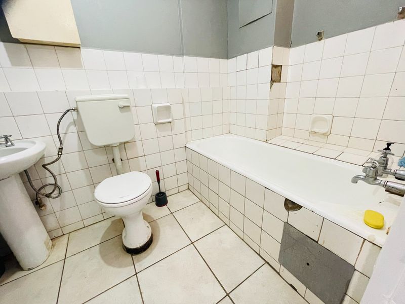 A dated bathroom featuring a pedestal basin, toilet, and bathtub with visible tile damage and maintenance requirements, offering potential for a full renovation.